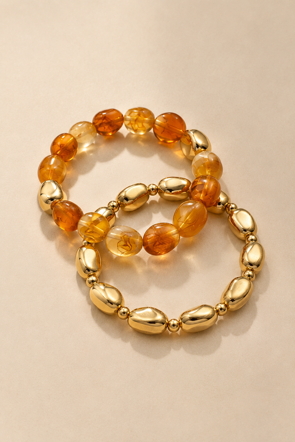 Amber and gold-tone stretch bracelet set layered on warm beige background