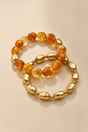 Amber and gold-tone stretch bracelet set layered on warm beige background