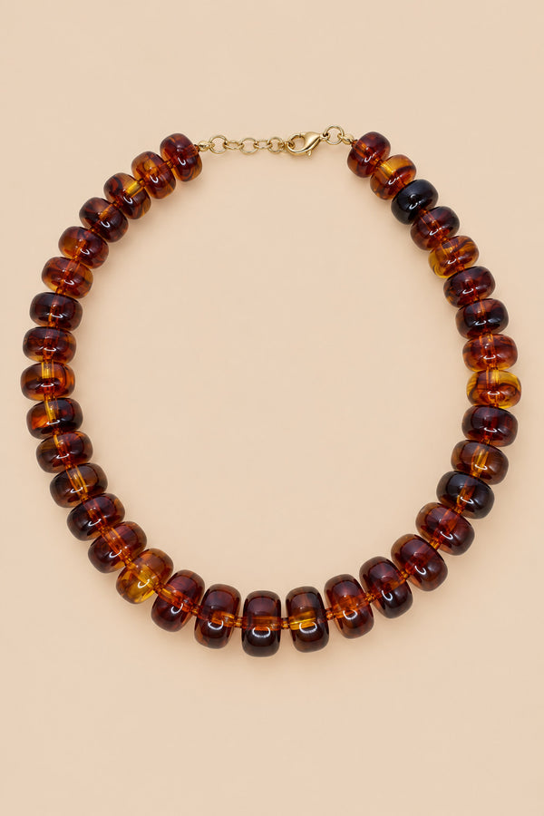 Brown translucent beaded necklace with gold-tone clasp on beige background
