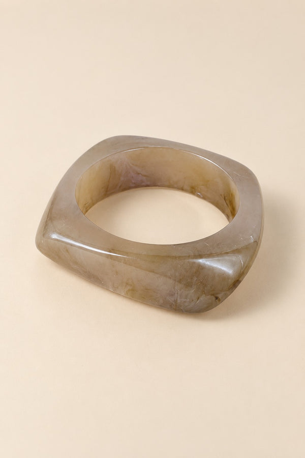 Close-up alternate view of the coffee-tone geometric resin bangle on beige.