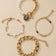 Gold-tone pearl bracelet set arranged naturally on a warm beige background.