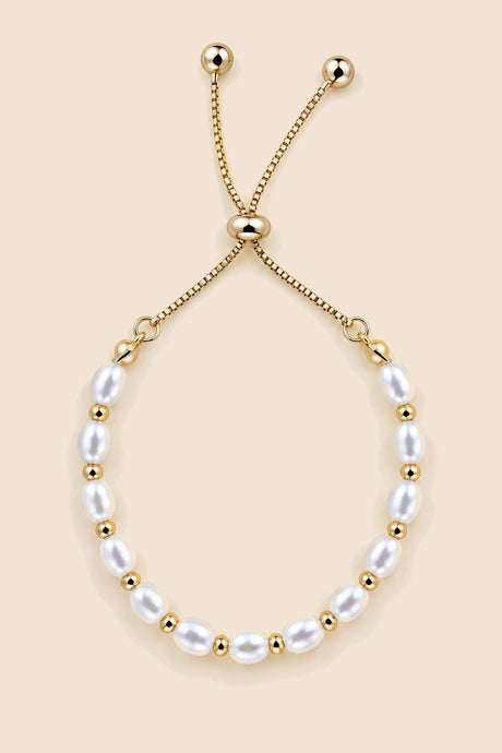 Gold-tone pearl slider bracelet on a beige background.