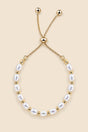 Gold-tone pearl slider bracelet on a beige background.