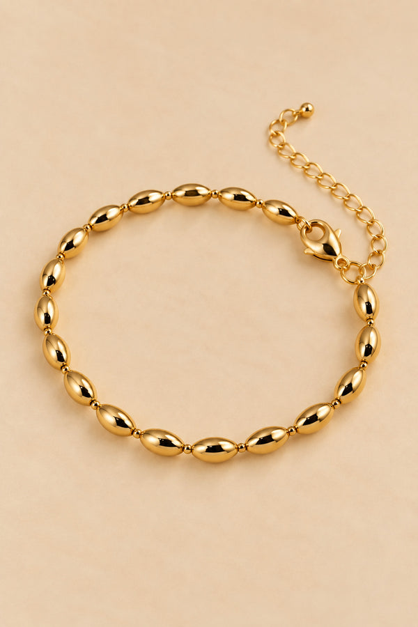 Gold-tone oval-bead bracelet on the ONZE warm beige accessory background.
