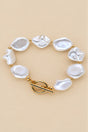 Irregular pearl bracelet with gold-tone spacers and toggle clasp on beige background.