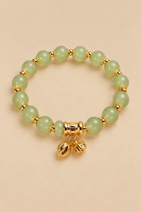 Pale green beaded charm bracelet with gold-tone charms on an ONZE beige background.