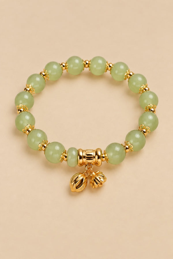 Pale green beaded charm bracelet with gold-tone charms on an ONZE beige background.