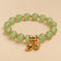 Pale green beaded charm bracelet with gold-tone details on an ONZE beige background.