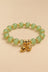 Pale green beaded charm bracelet with gold-tone details on an ONZE beige background.