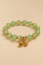 Pale green beaded charm bracelet with gold-tone details on an ONZE beige background.
