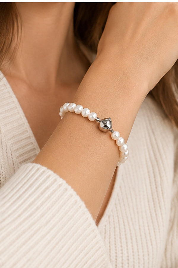 Irregular white pearl bracelet with silver-tone heart clasp worn on the wrist.
