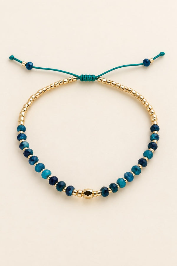 Teal beaded bracelet on a beige background.