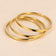 Gold-tone three-ring bangle set on a warm beige background.