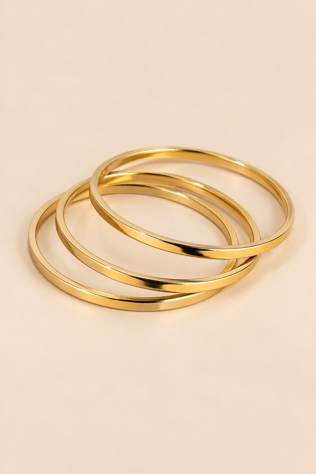 Gold-tone three-ring bangle set on a warm beige background.