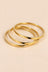 Gold-tone three-ring bangle set on a warm beige background.