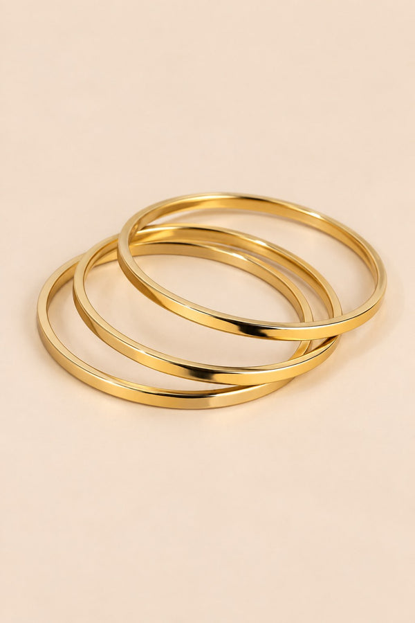 Gold-tone three-ring bangle set on a warm beige background.