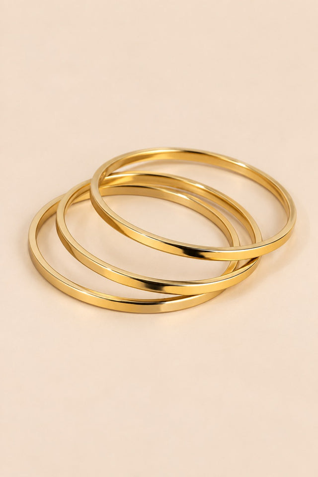 Gold-tone three-ring bangle set on a warm beige background.