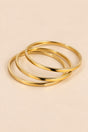 Gold-tone three-ring bangle set on a warm beige background.
